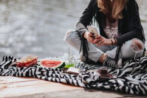 En kvinna sitter avslappnat på en filt  och studerar sin mobiltelefon. Framför henne liggen bland annat en melonklyfta. "Vem som helst kan lära var och när som helst."