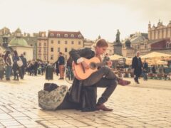 Gatumusikan sitter med gitarr på torg.