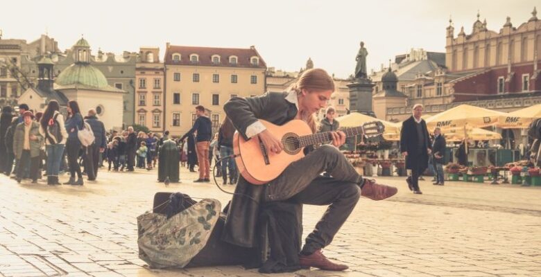 Gatumusikan sitter med gitarr på torg.